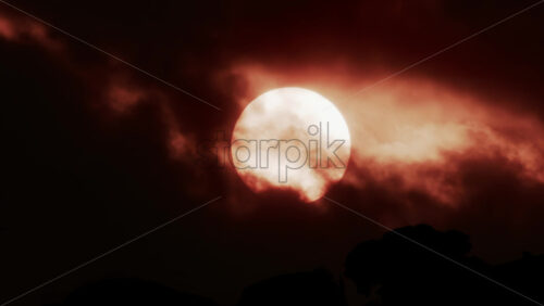 Video - A glowing red sun partially covered by dark clouds at dusk