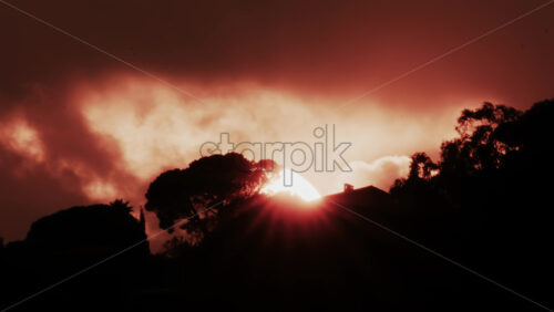 Video - A glowing red sun partially covered by dark clouds at dusk
