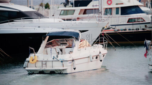 Video - A small white motorboat slowly sails out of the marina between larger yachts