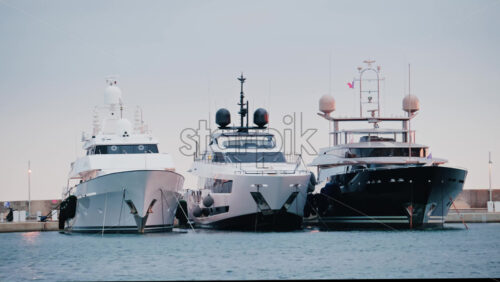 Video - Three luxury yachts docked side by side in a calm marina, captured in soft daylight