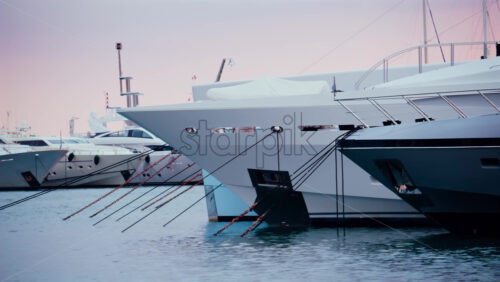 Video - Three luxury yachts docked side by side in a calm marina, captured in soft daylight