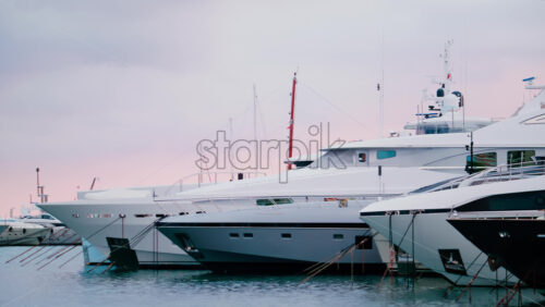 Video - Three luxury yachts docked side by side in a calm marina, captured in soft daylight