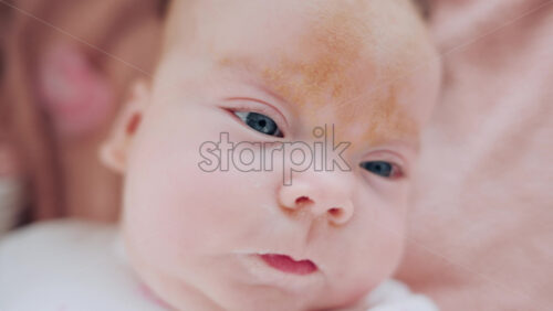 Video - A baby lies on a soft blanket, smiling and looking toward the camera