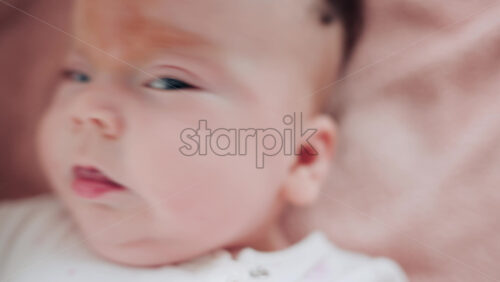 Video - A baby lies on a soft blanket, smiling and looking toward the camera