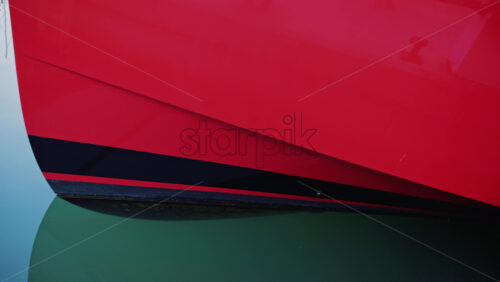 Video - Close up of a red and black boat hull reflecting on calm turquoise water