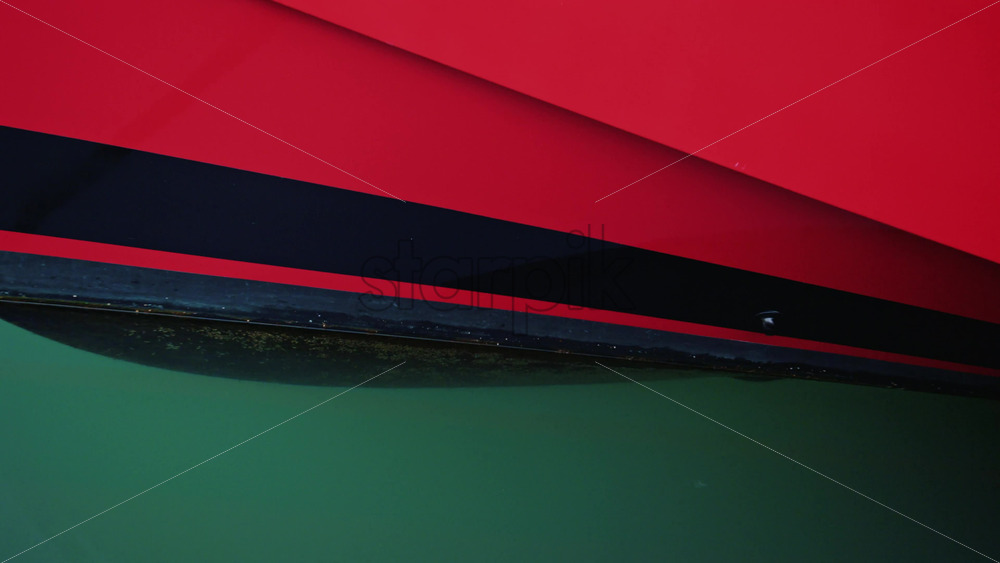 Video - Close up of a red and black boat hull reflecting on calm turquoise water