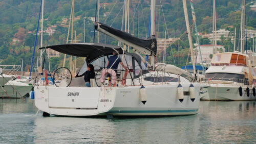 Video - Cannes, France - October 12, 2025: A man steering a white sailboat as it leaves a marina on a calm day