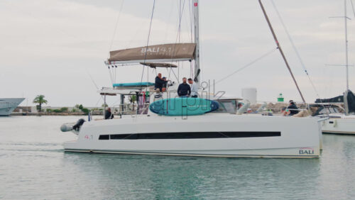 Video - Cannes, France - October 12, 2025: A man steering a white sailboat as it leaves a marina on a calm day
