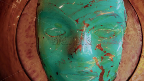 Video - Close up of a turquoise sculpted mask with gold paint details