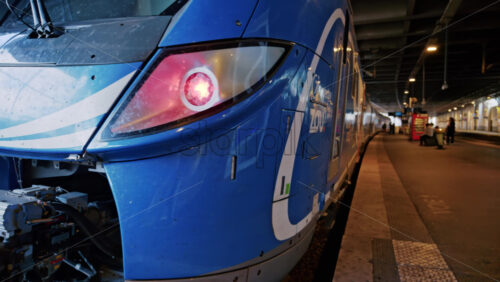 Video - Cannes, France - October 12, 2025: Close up of a modern blue train with red lights arriving at a covered railway platform