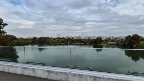 Video - Cannes, France - October 3, 2025: View of a calm city lake surrounded by trees with distant residential buildings under a cloudy sky