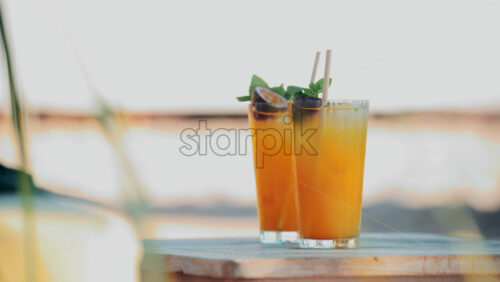 Video - Two bright orange cocktails with mint and passion fruit on a small wooden table at a beach club