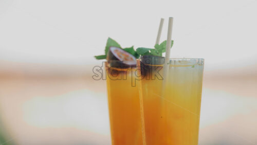 Video - Two bright orange cocktails with mint and passion fruit on a small wooden table at a beach club