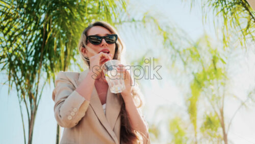 Video - Elegant woman holding a glass of lemon water while relaxing at a beach bar under palm trees