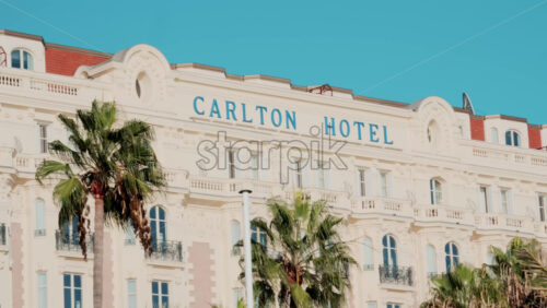 Video - Cannes, France - October 13, 2025: Elegant white facade of the iconic Carlton Hotel in Cannes, framed by palm trees and bright blue sky