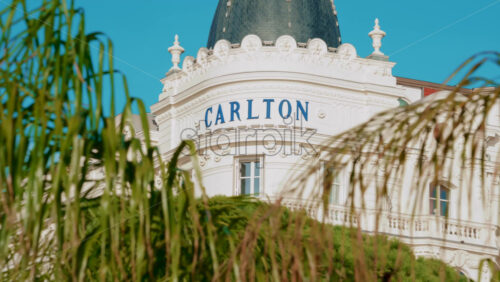 Video - Cannes, France - October 13, 2025: Famous dome of the Carlton Hotel seen through lush palm leaves, under a clear turquoise sky