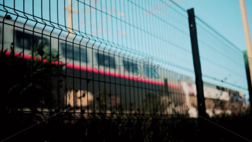 Video - Blurred motion of a modern train seen through a wire fence with blue sky background