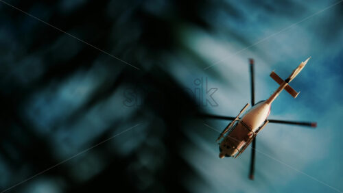 Video - View of a white helicopter flying across a blue sky framed by blurred palm trees