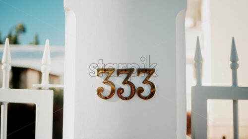 Video - Golden metallic number 333 mounted on a white wall in sunlight