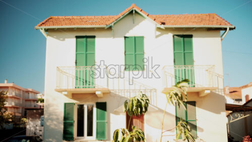 Video - Front view of a charming Mediterranean style house with green shutters and red tiled roof under clear blue sky
