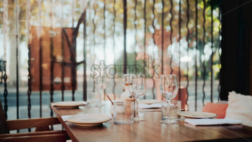 Video - Wooden restaurant table prepared with glasses, plates, and napkins in warm natural light