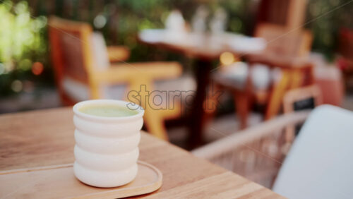Video - White ceramic cup of green matcha latte on a wooden table in a bright outdoor cafe