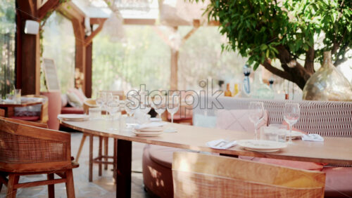 Video - Wooden restaurant table prepared with glasses, plates, and napkins in warm natural light