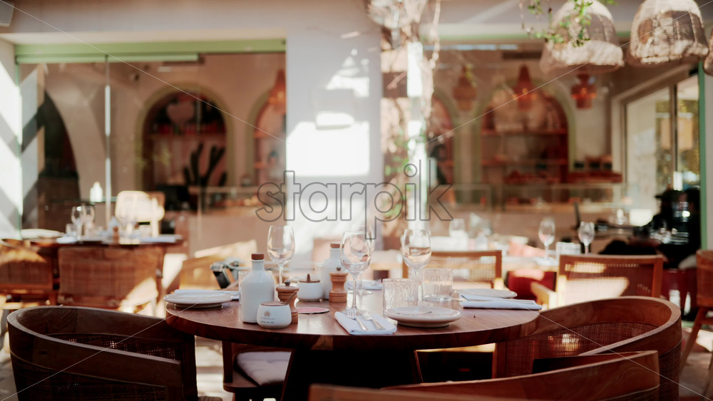 Video - Wooden restaurant table prepared with glasses, plates, and napkins in warm natural light