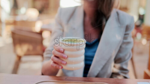 Video - Stylish woman wearing sunglasses enjoys a cup of matcha in a bright Mediterranean cafe