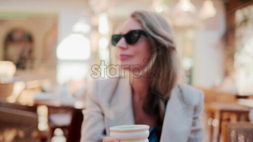 Video - Stylish woman wearing sunglasses enjoys a cup of matcha in a bright Mediterranean cafe
