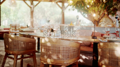Video - Wooden restaurant table prepared with glasses, plates, and napkins in warm natural light