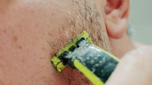 Video - Close up of a man using an electric razor to trim facial hair in the bathroom