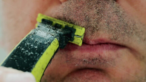 Video - Close up of a man using an electric razor to trim facial hair in the bathroom