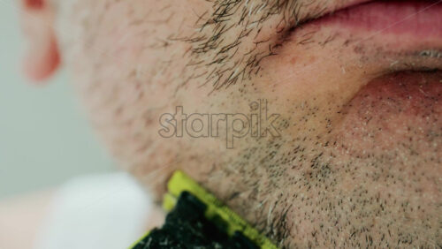 Video - Close up of a man using an electric razor to trim facial hair in the bathroom