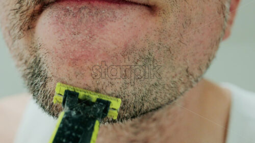 Video - Close up of a man using an electric razor to trim facial hair in the bathroom