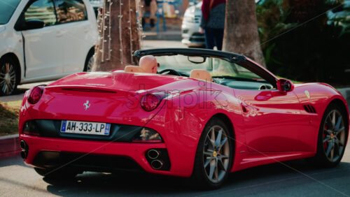 Video - Cannes, France - October 3, 2025: Red convertible Ferrari car driving through sunny city streets with palm trees and traffic