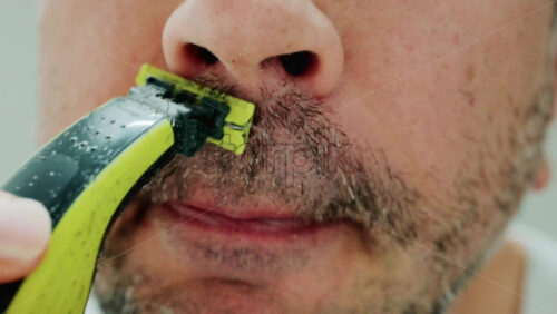 Video - Close up of a man using an electric razor to trim facial hair in the bathroom