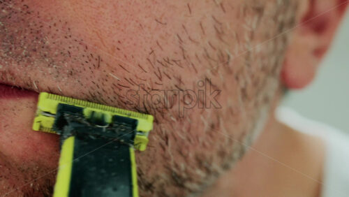 Video - Close up of a man using an electric razor to trim facial hair in the bathroom