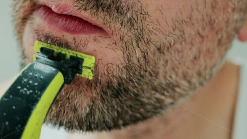 Video - Close up of a man using an electric razor to trim facial hair in the bathroom