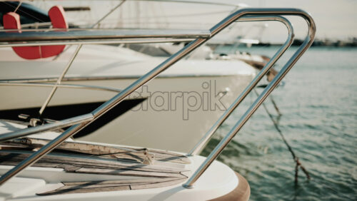 Video - Close up of chrome railing and wooden deck of a luxury yacht docked in a marina under golden light