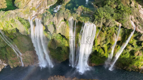 Video – Aerial drone view of Tamul Waterfall cascading down green cliffs into a turquoise pool below - Starpik Stock