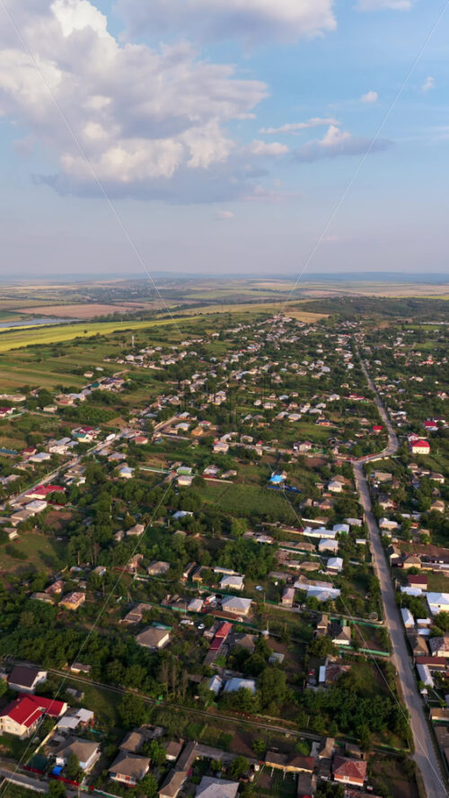 Video – Aerial drone view showing a Moldovan village surrounded by vast farmlands and open fields under a hazy autumn sky. Vertical - Starpik Stock