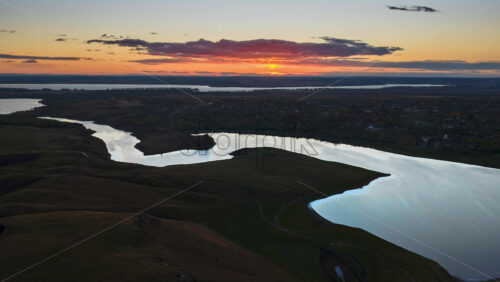 Video - Aerial drone view of a winding river reflecting the warm sunset light over Moldova's rolling hills and distant villages time lapse