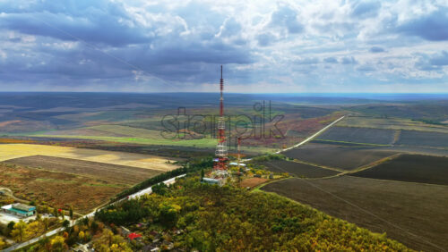 Video - Aerial drone view of a tall radio transmission tower rising above Moldovan farmlands under a dramatic cloudy sky