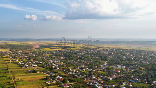 Video - Aerial drone view of the vast Moldovan countryside with colorful patchwork fields stretching to the horizon under a partly cloudy summer sky