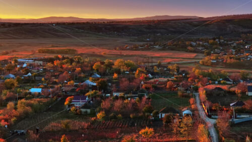 Video - Aerial drone view of a Moldovan village surrounded by autumn trees and farmlands during sunset