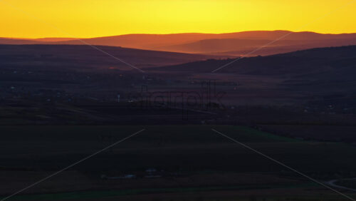 Video - Aerial drone view of Moldova's rolling hills at dusk, layered in soft light with a glowing yellow orange sky