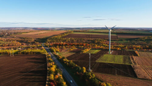 Video - Aerial drone view of a wind turbine standing tall in Moldovan farmland surrounded by colorful autumn trees