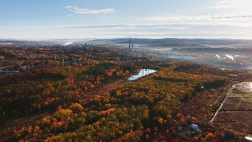 Video - Aerial drone view of a Moldovan city bordered by autumn colored forests and a river, with distant industrial chimneys