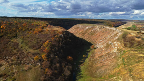 Video - Aerial drone view of Moldova's hilly canyon landscape, with patches of autumn trees and winding trails